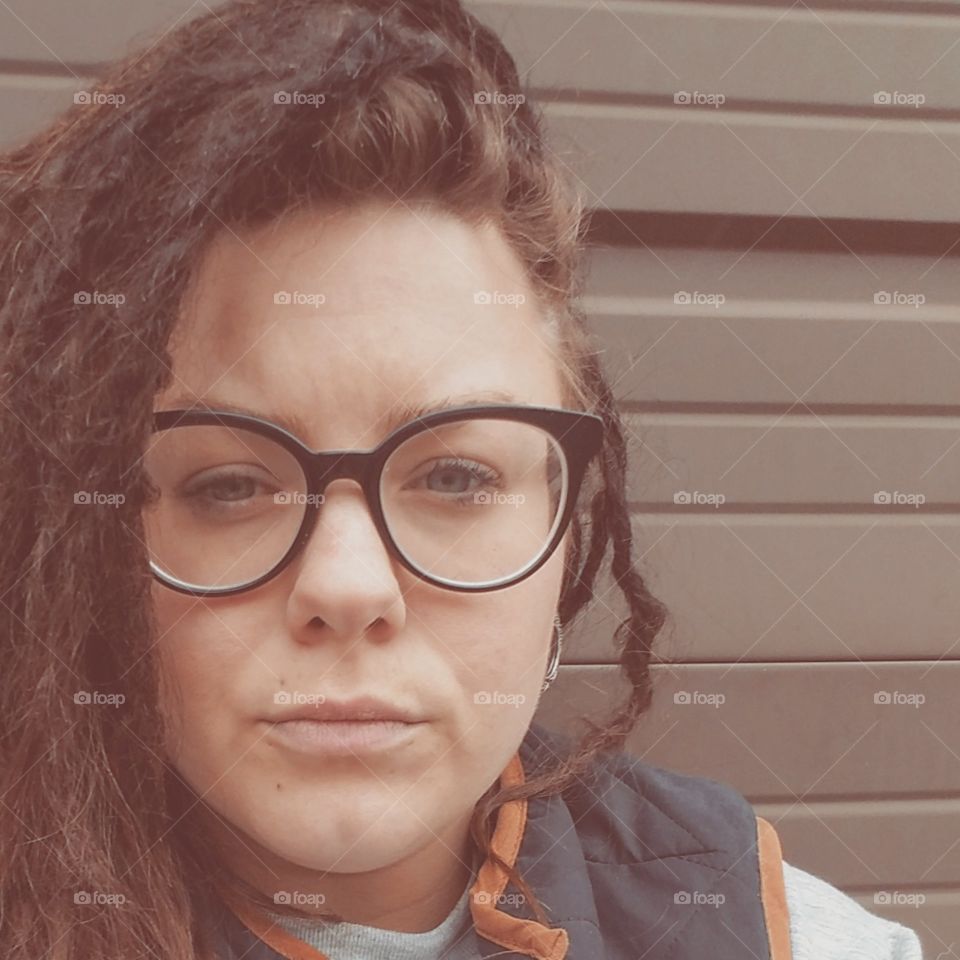 Stoic woman with eyeglasses and dreadlocks. Brunette.