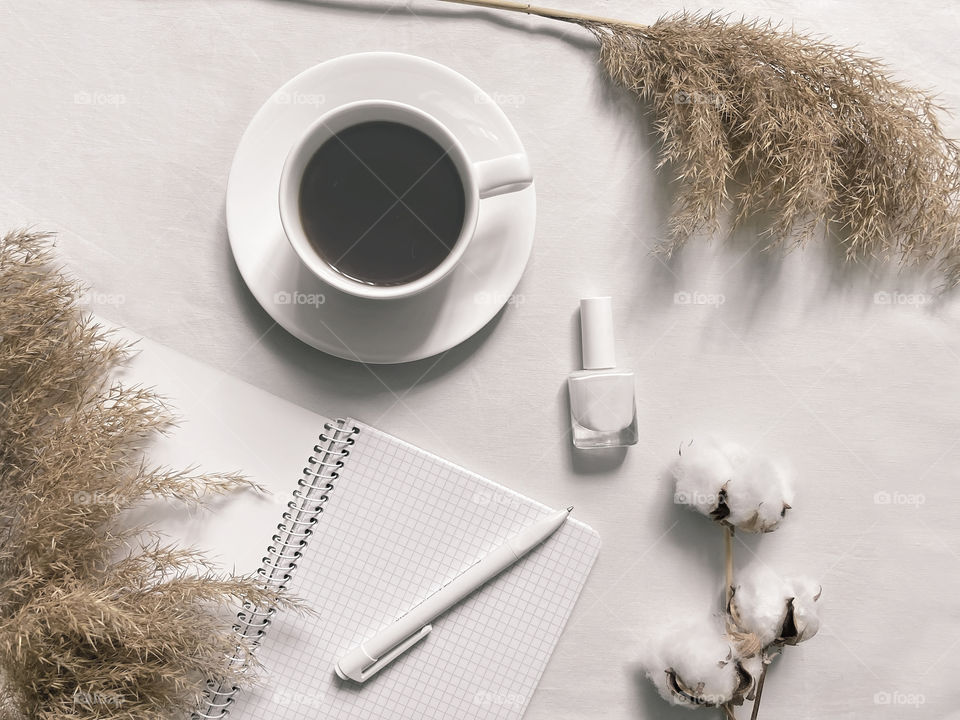 Coffee cup on white desktop with notes and white nail polish 