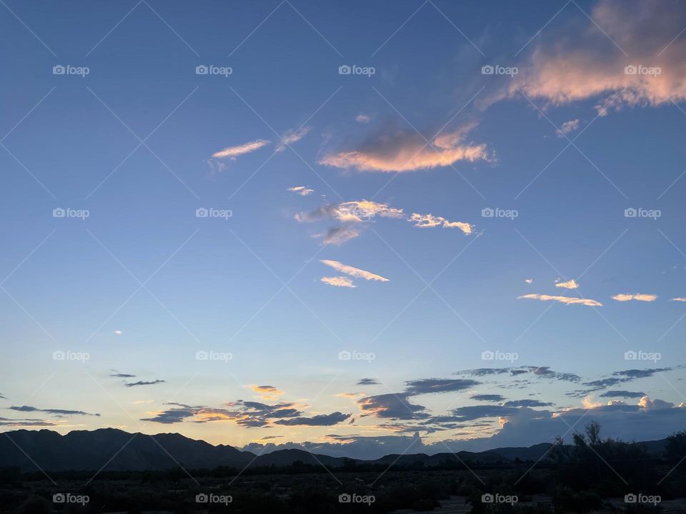 A colorful sunset with mountains and light pink clouds above the sunset.        