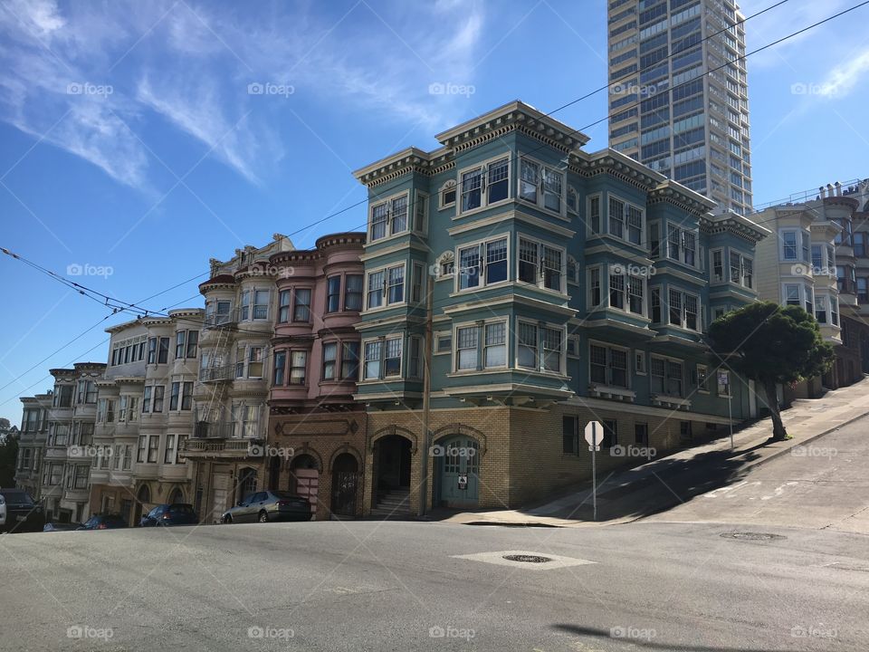 Corner street shot. San Francisco homes. Green, pink, yellow. Blue skies. 