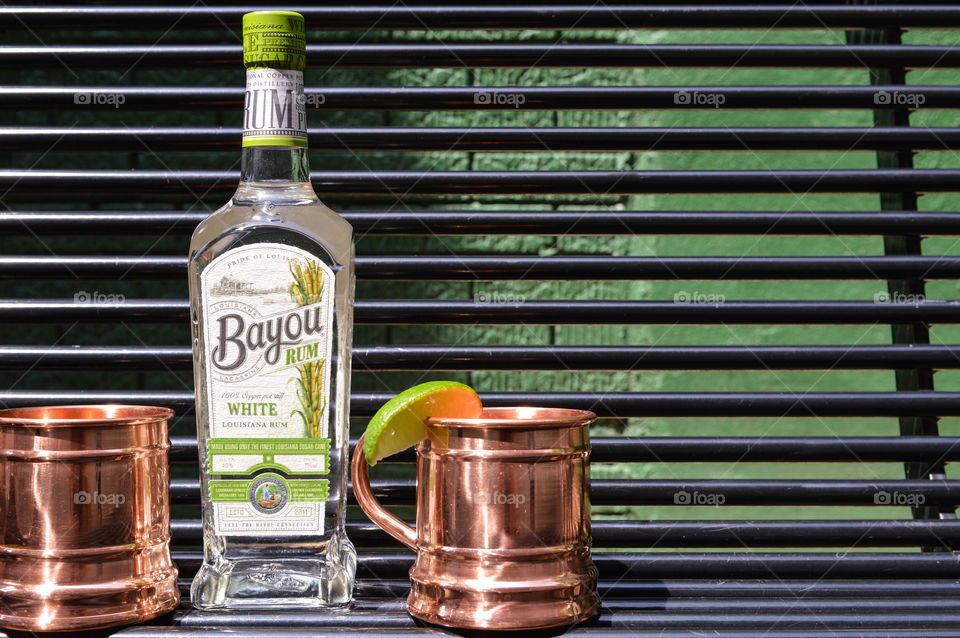 Bottle of Bayou white rum on a bench with two copper mugs