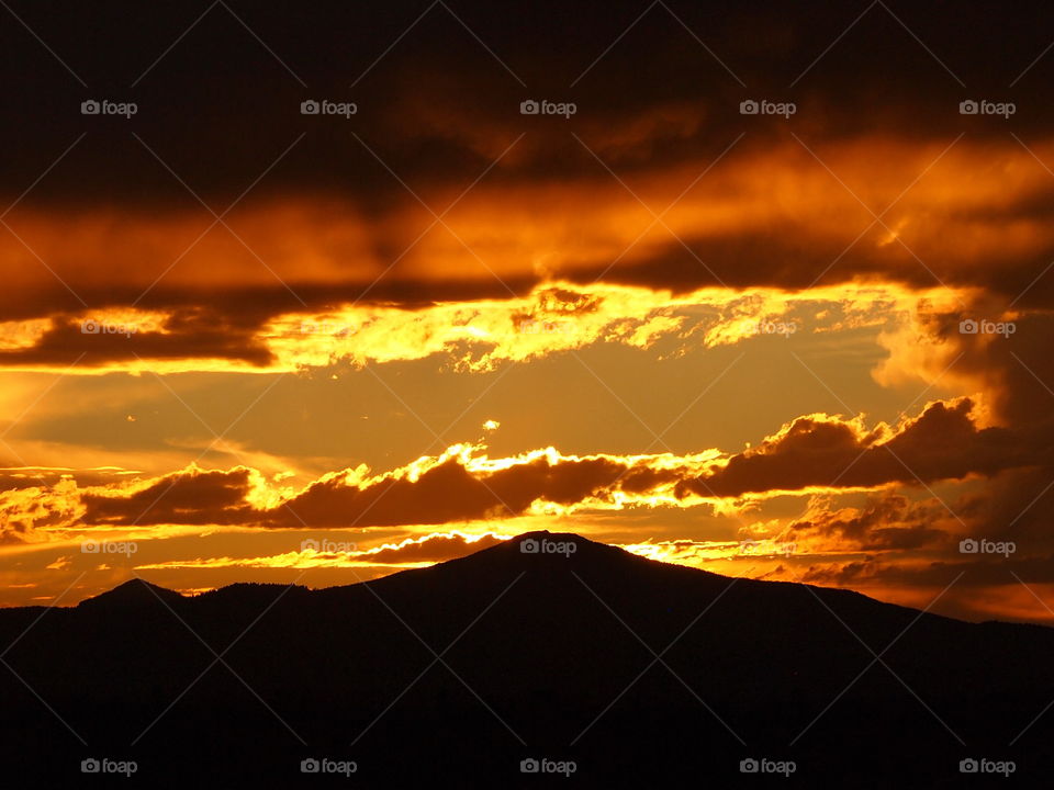 The Central Oregon Cascade Mountain Range at sunset after a storm causing different colors of red, yellow, gold, and, orange in the different layers of clouds. 