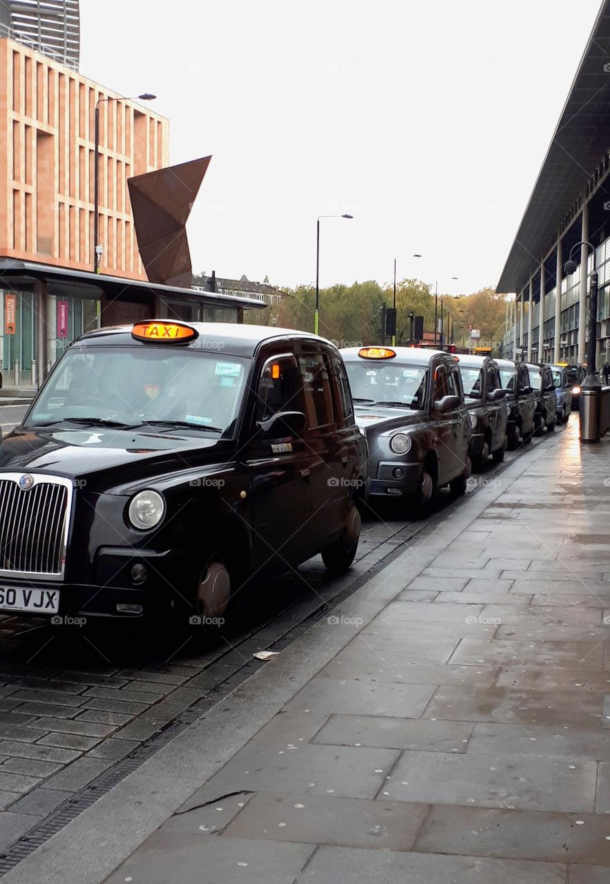 Line of elegant black london taxis parked along sidewalk.