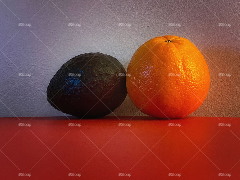 An orange and an avocado on a red table