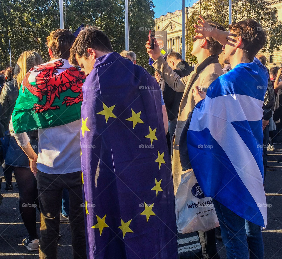 3 young men stand with the Welsh, Scottish and EU flags draped around them, listening to speeches at the People’s Vote March in London, 20th October 2018