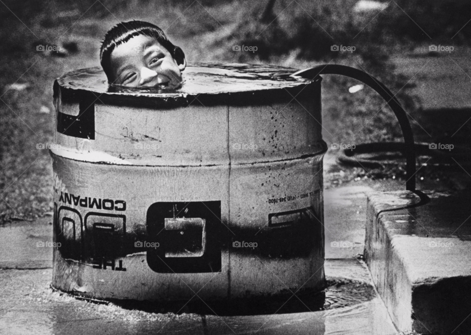 young boy cools off in a cut-down 50 gallon drum filled by a garden hose in a phoenix barrio. barrio. arizona by arizphotog