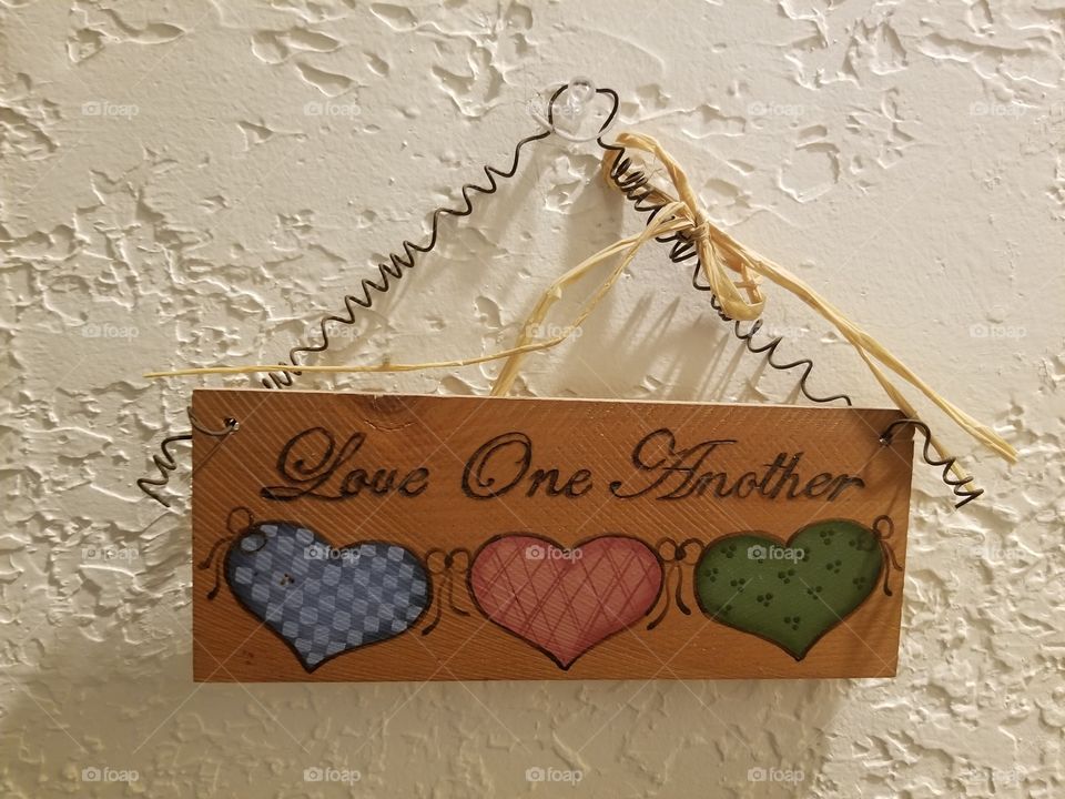 "love one another" sign hangs on spiral wire with a white bow. wall art, decoration