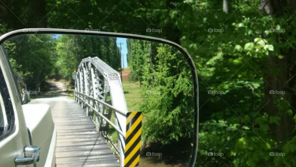 Rearview Sideview mirror of old bridge with wooden road