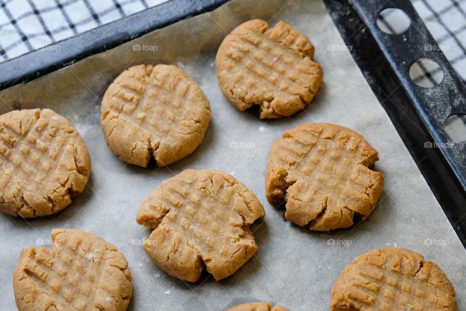 Close up of baked American peanut butter cookies on a baking sheet lined with baking paper laying on a checkred napkin