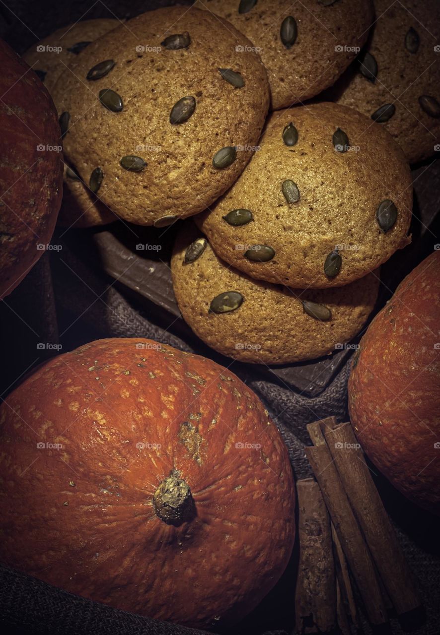 Tasty, soft pumpkin cookies surrounded by orange pumpkins and cinnamon against rustic cloth and dark wood background 