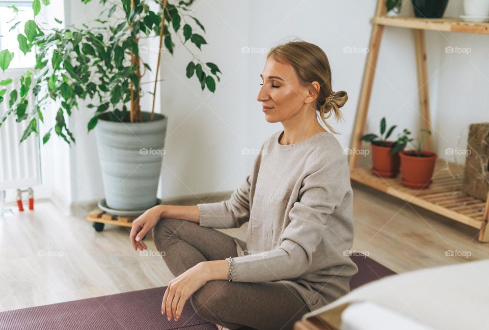 Beautiful blonde young woman in comfortable sport wear practice yoga in cozy bedroom at home