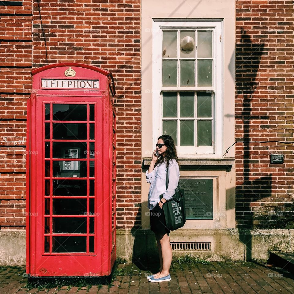 Young woman talking on mobile phone near telephone booth