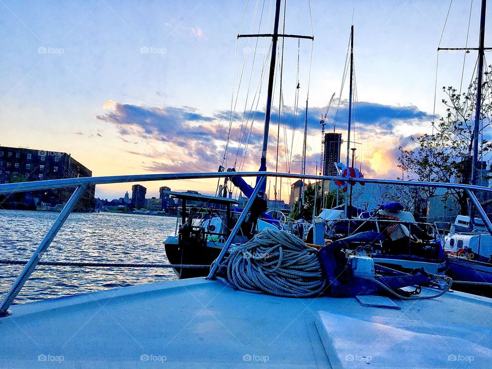 A twilight time view from aboard the “Salvation” of the “harbor area” at Newtown Creek in LIC, Queens, NY with various sailboats and other boats anchored by the shoreline. 2021. Hypnotic Productions