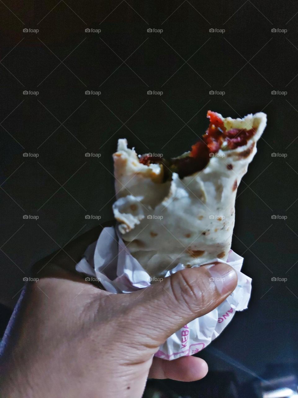 A man's hand shows a partially bitten kebab dish against the background of the night sky