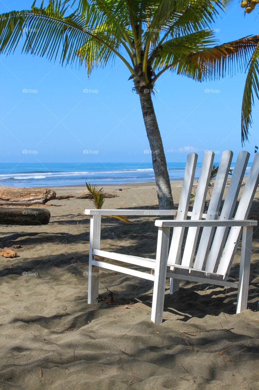 A perfect vacation.  An empty sandy beach a wooden chair in the shade by the sea.  Palosecobeach,  Costa Rica