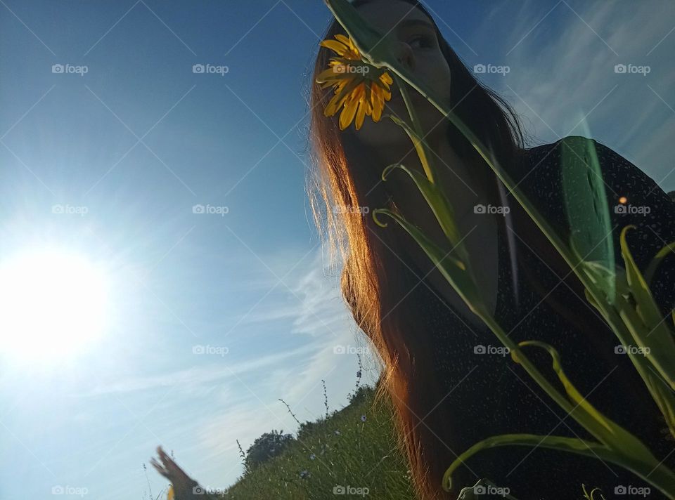 It is a photo of a young woman in the field. She has red (ginger) hair. She has brown eyes. Her face is partly coverd with Tragopogon pratensis (common names Jack-go-to-bed-at-noon, meadow salsify, showy goat's-beard or meadow goat's-beard)