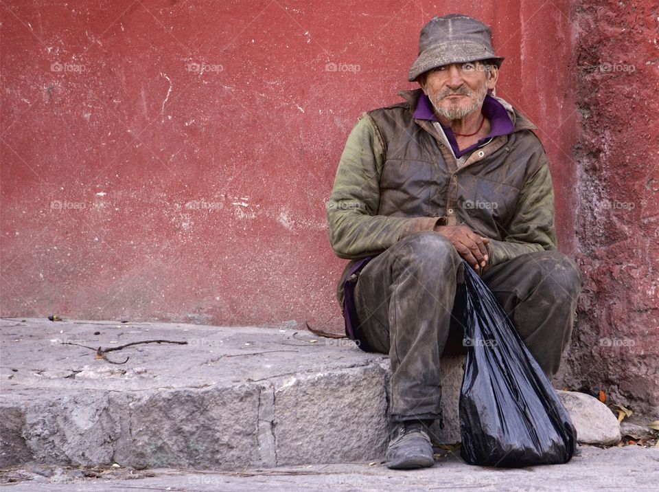 A man is seated on the the sidewalk in San Miguel de ale de, Mexico.
