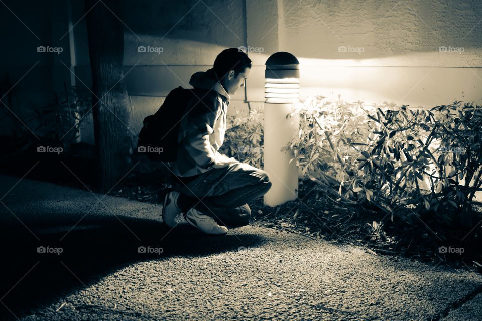 Young man crouching in front of lighting on street