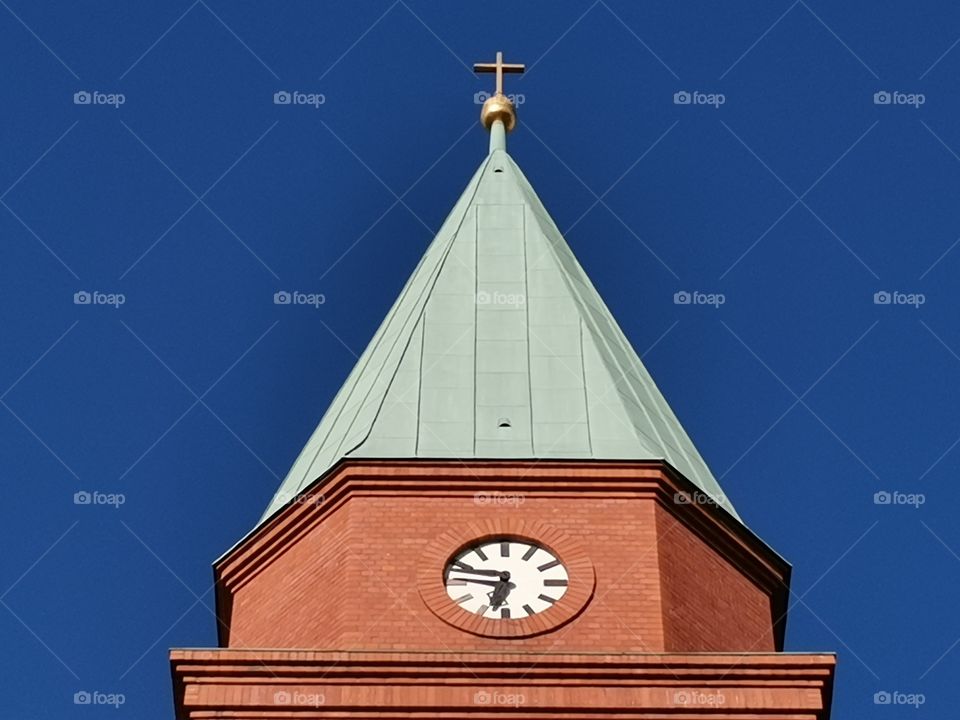 Part of a brick church tower with a clock in the center and a blue sky in the background