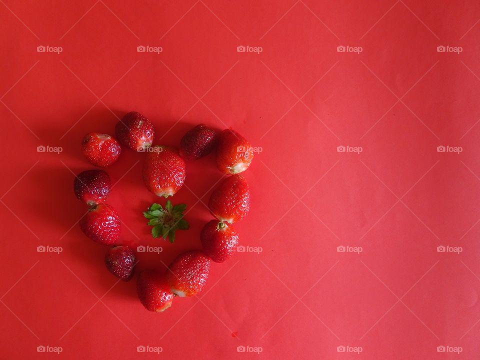 heart shaped made with strawberries on red background
