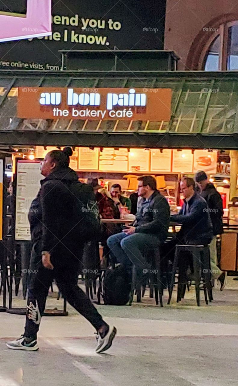 Men sitting at small food stand as woman rushes by on her way to trains. The train station has no trains coming in at the moment, so there's no crowd.