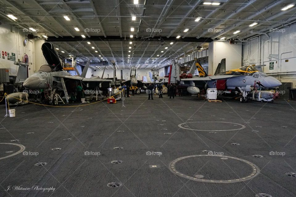 F/A-18 Super Hornets receive maintenance aboard an aircraft carrier