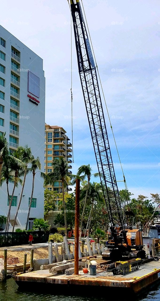 Crane on barge with construction materials for building on the river. There's are highrise condos along side near this barge.