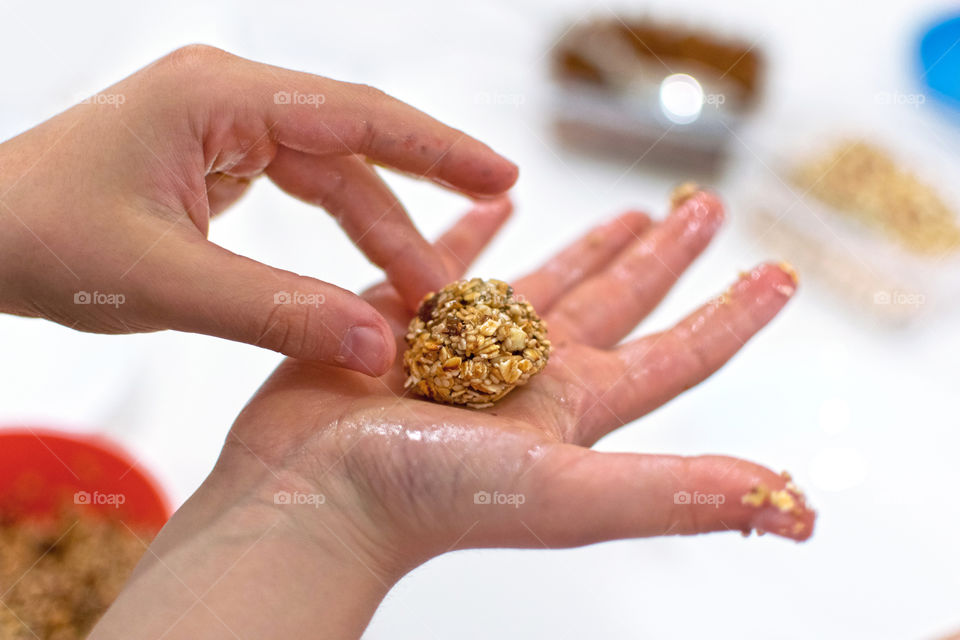 Children's hands making balls of oats with raisins and almonds and honey.
