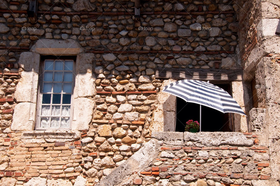 A striped umbrella in front of an old stone building in France