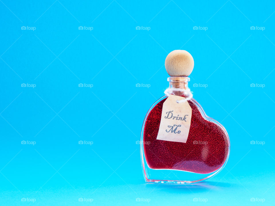 Love potion in a heart-shaped bottle with blue background 