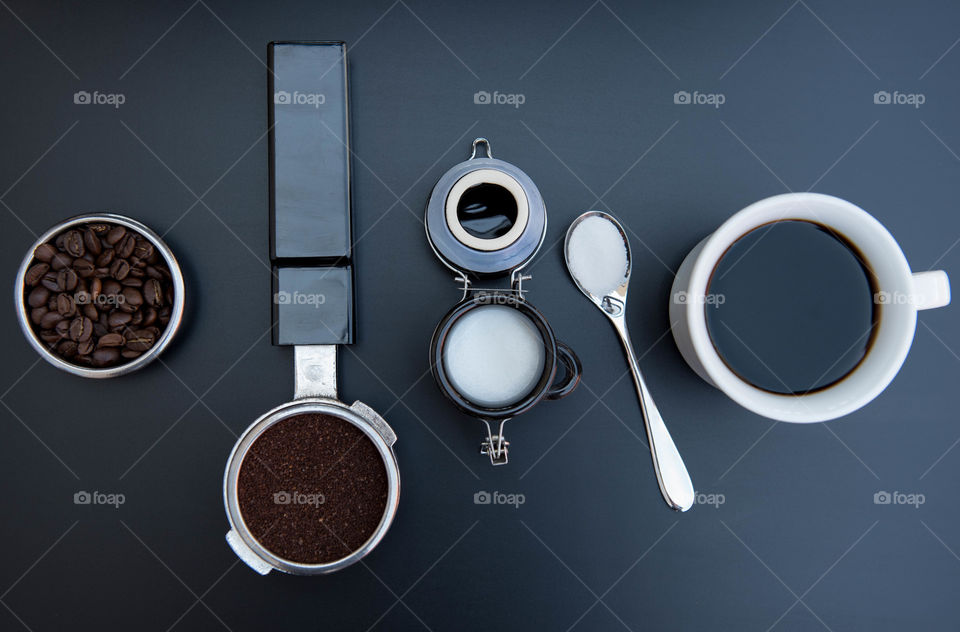 Monochromatic flat lay of a cup of coffee, coffee beans, coffee grounds and sugar