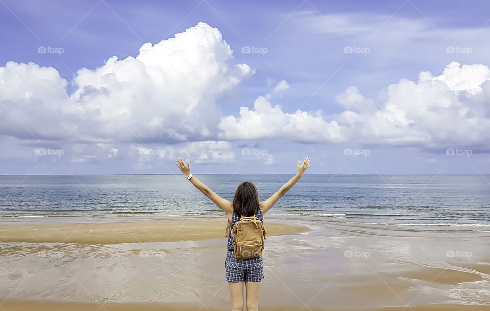 Women raise their arms and shoulder backpack on the beach background sea and sky.