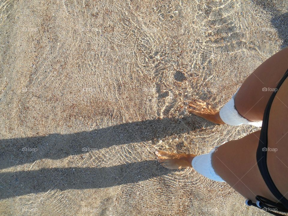 female legs on a clear water sea sand shore top view