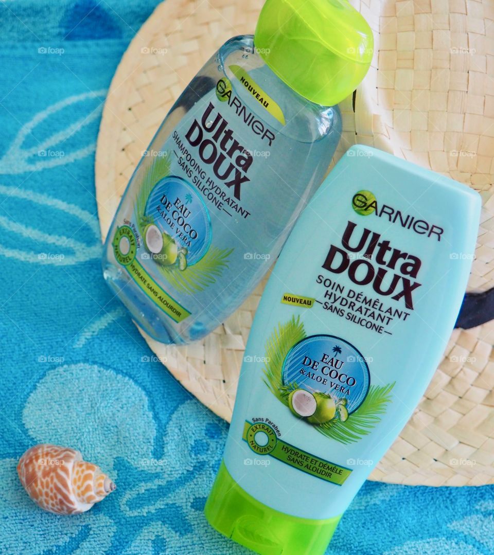 Garnier eau de coco shampoo and conditioner on a blue beach towel with a seashell and straw hat.