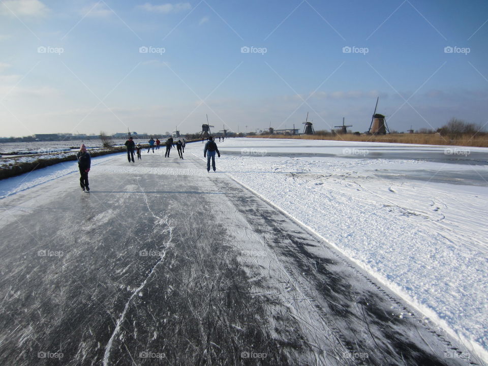 Ice skating on frozen canal next to wind mills