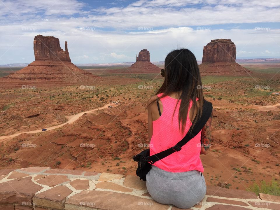 A beauty tourist is sitting on the fence of Monument valley visitor center and look around from her