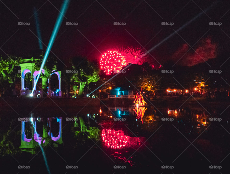 Night view of an illuminated bandstand on a pond with lasershow and a firework during a light festival.