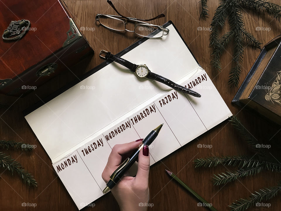 Female hand holding a pen over the calendar on brown wooden table 