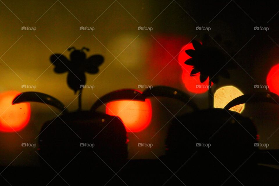 Silhouette photo of a flower in a vase on a blurry light background at night.