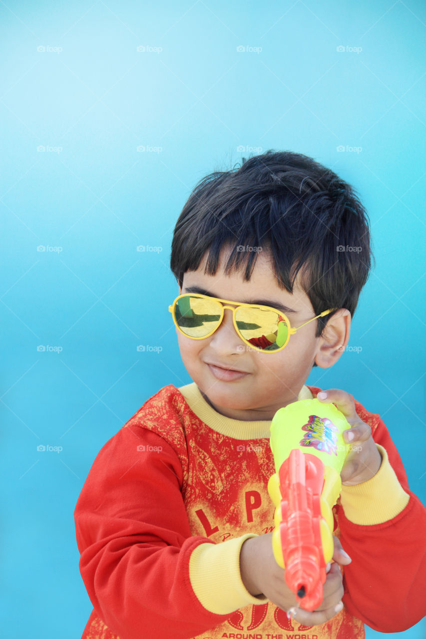 Smiling Indian boy celebrating holi festival with a water gun - festival of colors