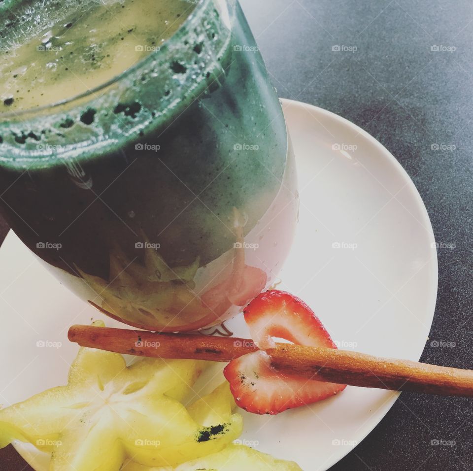 Beautiful colorful smoothie with pink, white and green on plate ready to drink next to heart shaped strawberry, star fruit and cinnamon stick 
