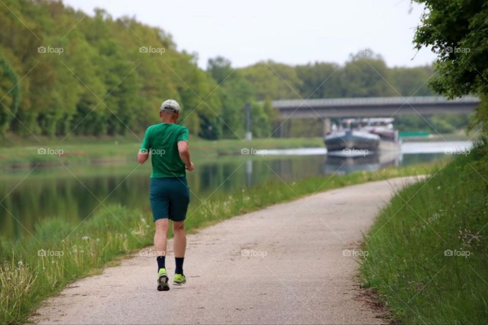 Rear view of a running man along a canal with a ship