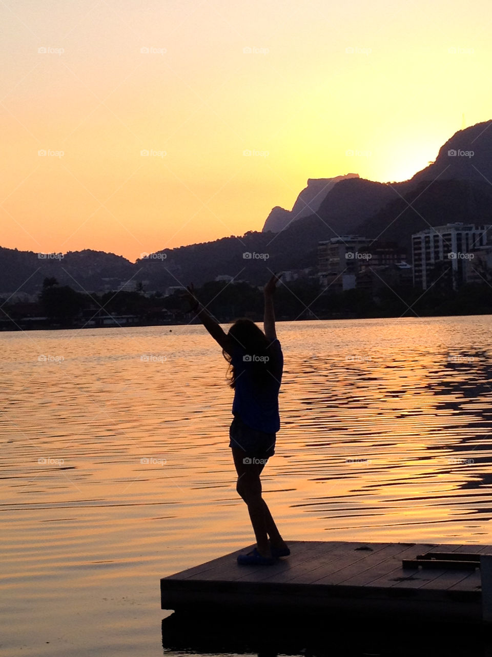 A girl with arms up by a lake in a beautiful sunset