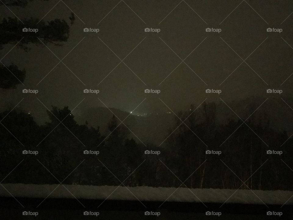 A foggy winter evening in Norway. You see the lights from the other side of the fjord. About 1-2 centimeters of snow has layed onto the fence.