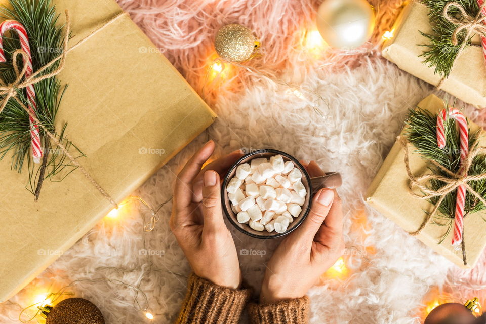 Female hands holding cup of cocoa with marshmallows. Flat lay items 