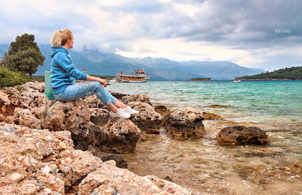 Girl sits on the shore and looks at the sea