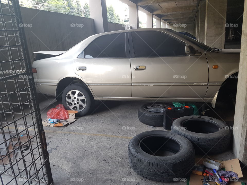 Broken car with missing wheel under repair in a dusty garage