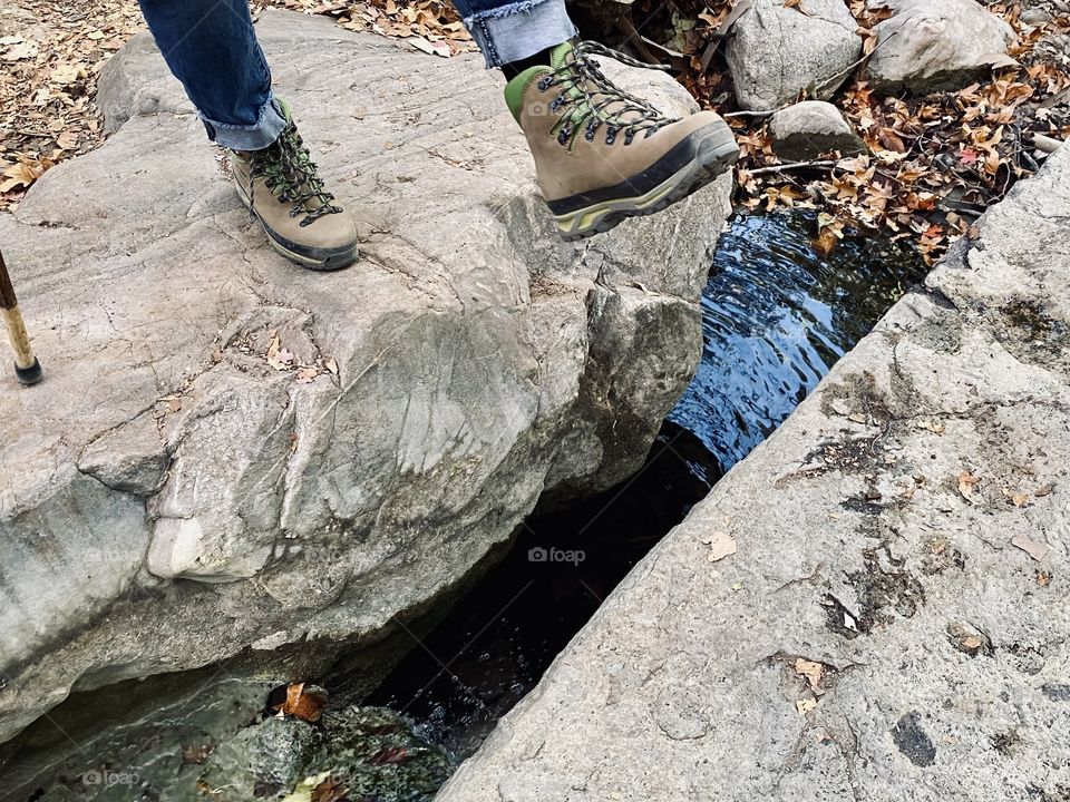 Woman hiking and crossing a rock crevice over the stream of water
