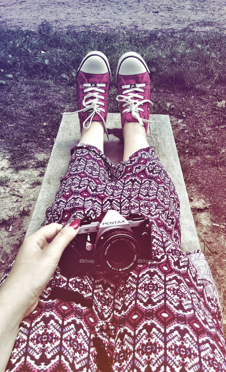 Woman holding vintage camera on her knees while sitting on a wooden bench in the forest