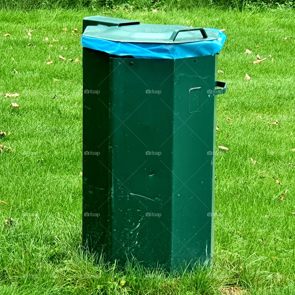 A green trash can for waste on the street.